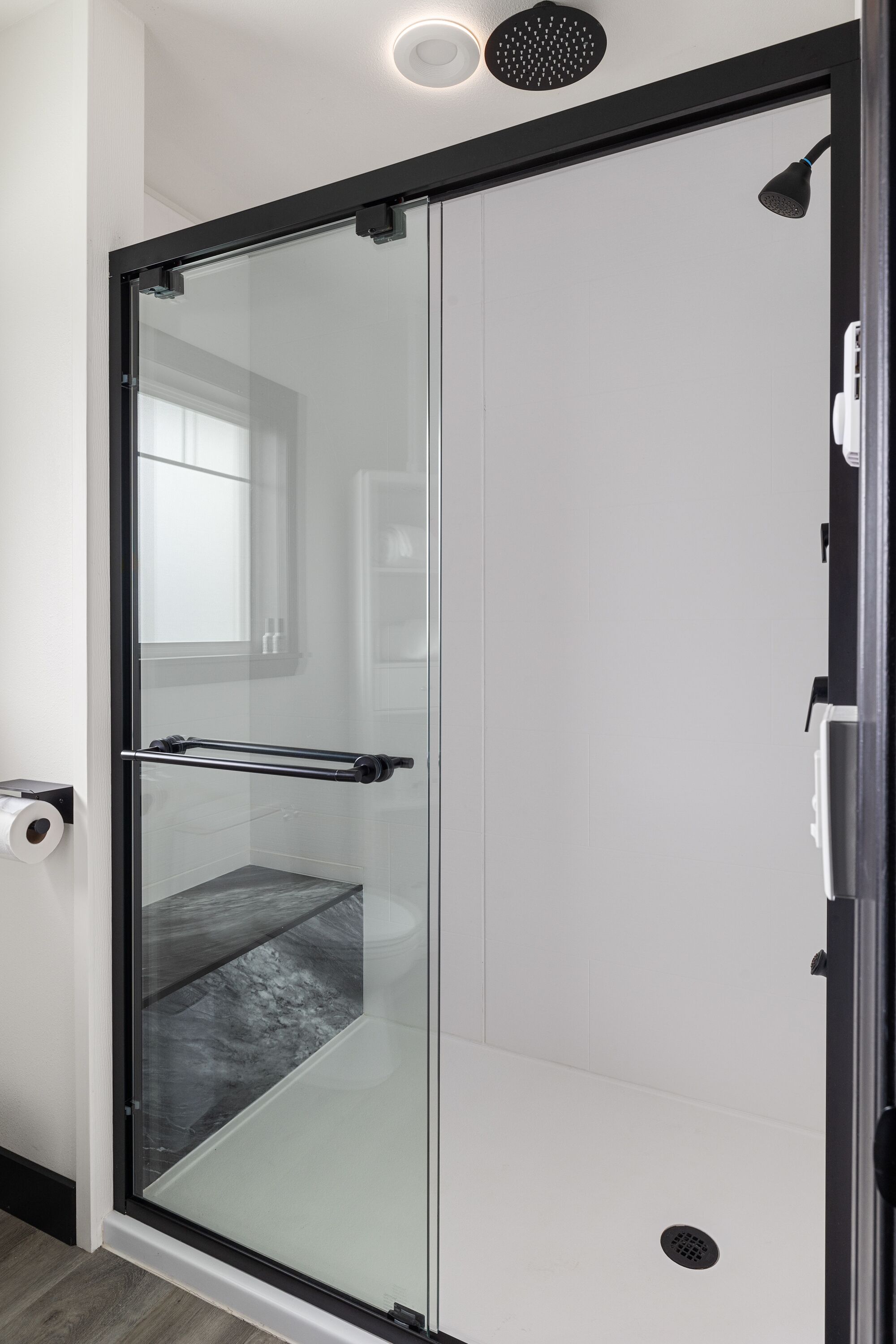 A modern shower with a glass door, a towel rack, and a ceiling-mounted showerhead.