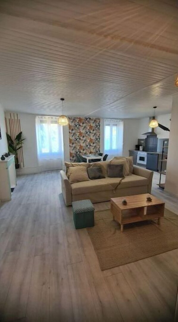 A spacious living room with a sofa, ottoman, and coffee table. There is a kitchen area with a stove and cabinets in the background.