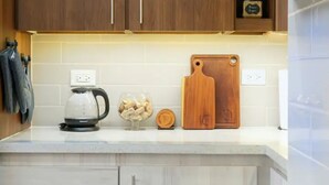 Una cocina con armarios blancos, una tetera, una tabla de cortar y un bol de fruta.