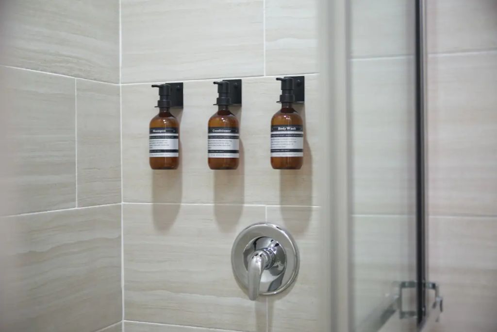 Ein Badezimmer mit drei Flaschen Shampoo und Conditioner an einem wandmontierten Spender.