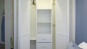 Un armario blanco con puertas correderas, varios estantes y cajones.