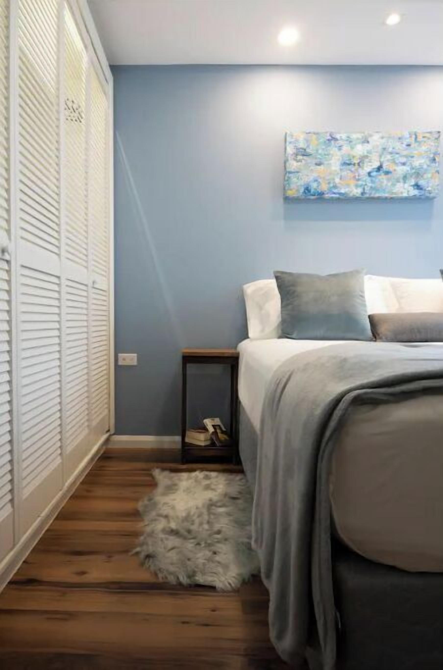 A bedroom with a bed, a nightstand, a fluffy rug, and a painting on the wall.