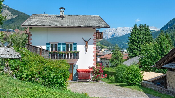 A mountain lodge with a wooden balcony, a crucifix, and a view of snow-capped mountains.