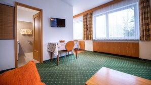 A hotel room with a dining table, chairs, a television, a window with curtains, and a green patterned carpet.