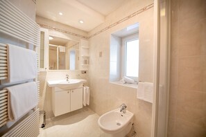 A modern bathroom with a sink, bidet, and a large mirror. - Central Apartments Cristlpek 184B (Ortisei)