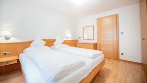Ein Hotelzimmer mit Doppelbett, Holz-Kopfteil, Nachttischen mit Lampen, einem Holzschrank und einem Spiegel an der Wand.