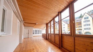 Ein Korridor mit Holzdielen und großen Fenstern, der zu einer Tür führt.