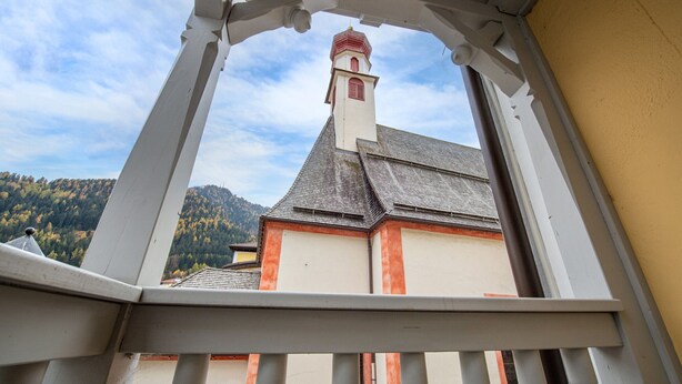 Ein Balkon mit Blick auf eine Kirche mit roten Ziegeldächern und einem Glockenturm.