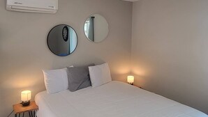 A bedroom with a large bed, two bedside tables with lamps, a ceiling light fixture, and two wall-mounted mirrors.