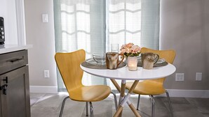 A dining area with a round table, two chairs, a vase with flowers, and two owl-themed mugs.