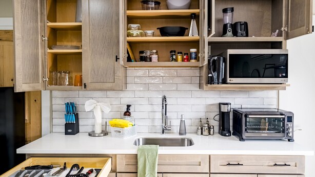 A kitchen with wooden cabinets, a white countertop, a sink, a toaster, and various kitchen utensils.