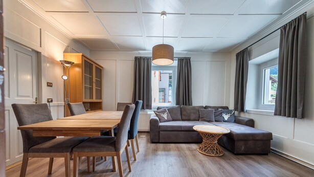 Un salon moderne avec une table à manger en bois, des chaises grises à revêtement, un canapé gris et une table basse ronde.