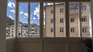 Une pièce dotée de grandes fenêtres donnant sur des bâtiments européens traditionnels et sur une montagne.