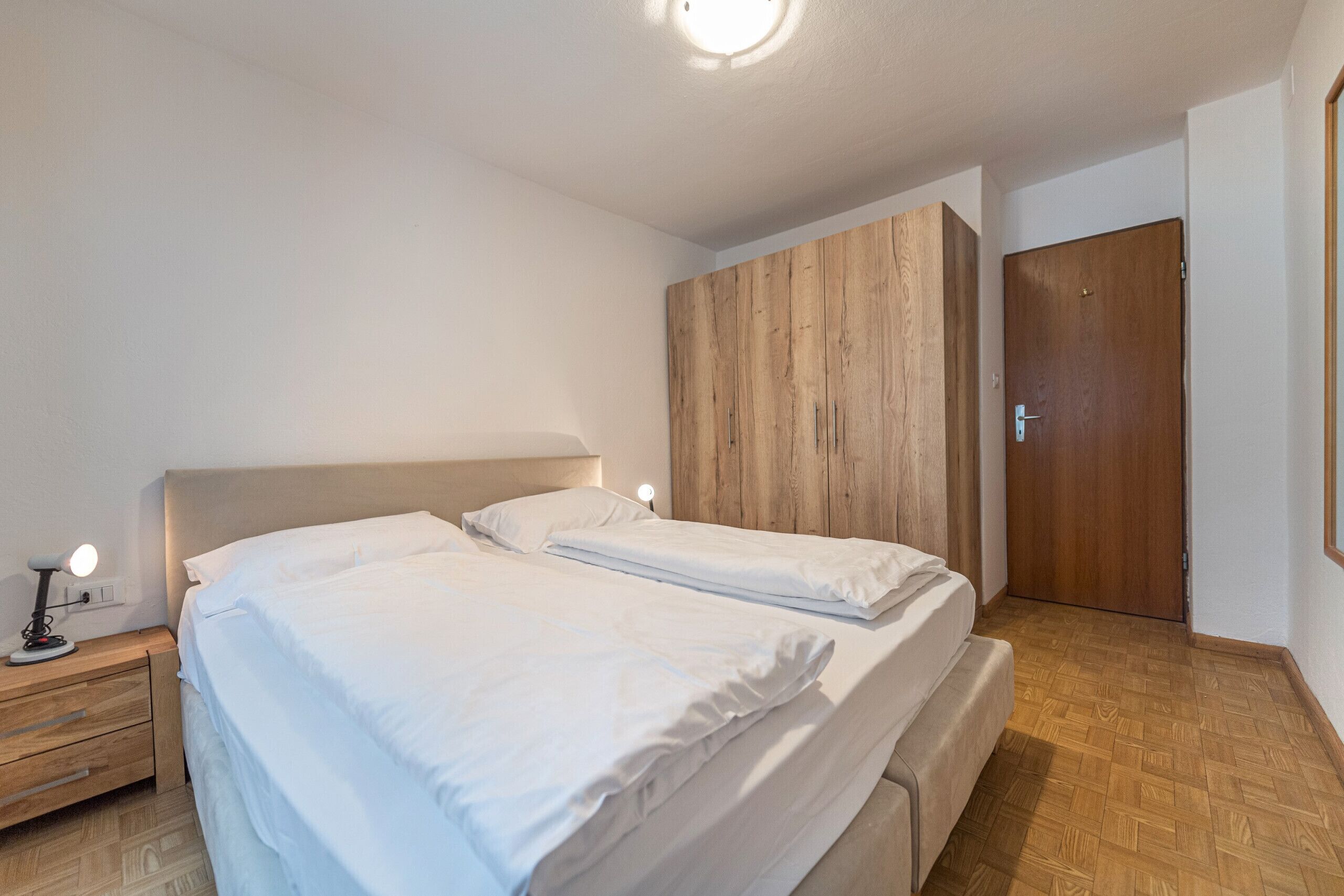 Een slaapkamer met een bed, nachtkastjes, een houten kledingkast en een deur.