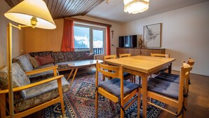 Un salón acogedor con un sofá, una mesa de comedor de madera y sillas. Hay un televisor y una cruz en la pared.