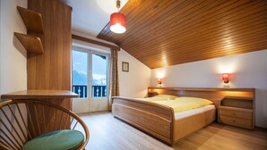 Un dormitorio con una cama de madera, una silla, un escritorio y vistas al exterior.