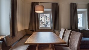 Ein Essbereich mit Holztisch und Bänken, einer Hängeleuchte und Blick auf Gebäude durch ein Fenster.