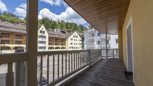 Ein hölzerner Balkon mit Geländer, der auf eine Straße mit Gebäuden und Bäumen blickt.