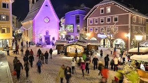 Ett snötäckt torg med historiska byggnader, en kyrka och en julmarknad.