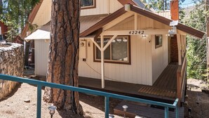A two-story wooden cabin with a balcony, a large tree in front, and a clear sky. - Cavu Cabin - A Classic Mountainside Escape (Shaver Lake)