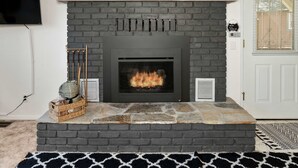 A fireplace with a stone surround, a mounted television, and a basket of items on the mantel. - Cavu Cabin - A Classic Mountainside Escape (Shaver Lake)