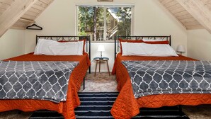 A room with two beds, a small table, a hanging light, and a window with a view of trees and a building. - Cavu Cabin - A Classic Mountainside Escape (Shaver Lake)