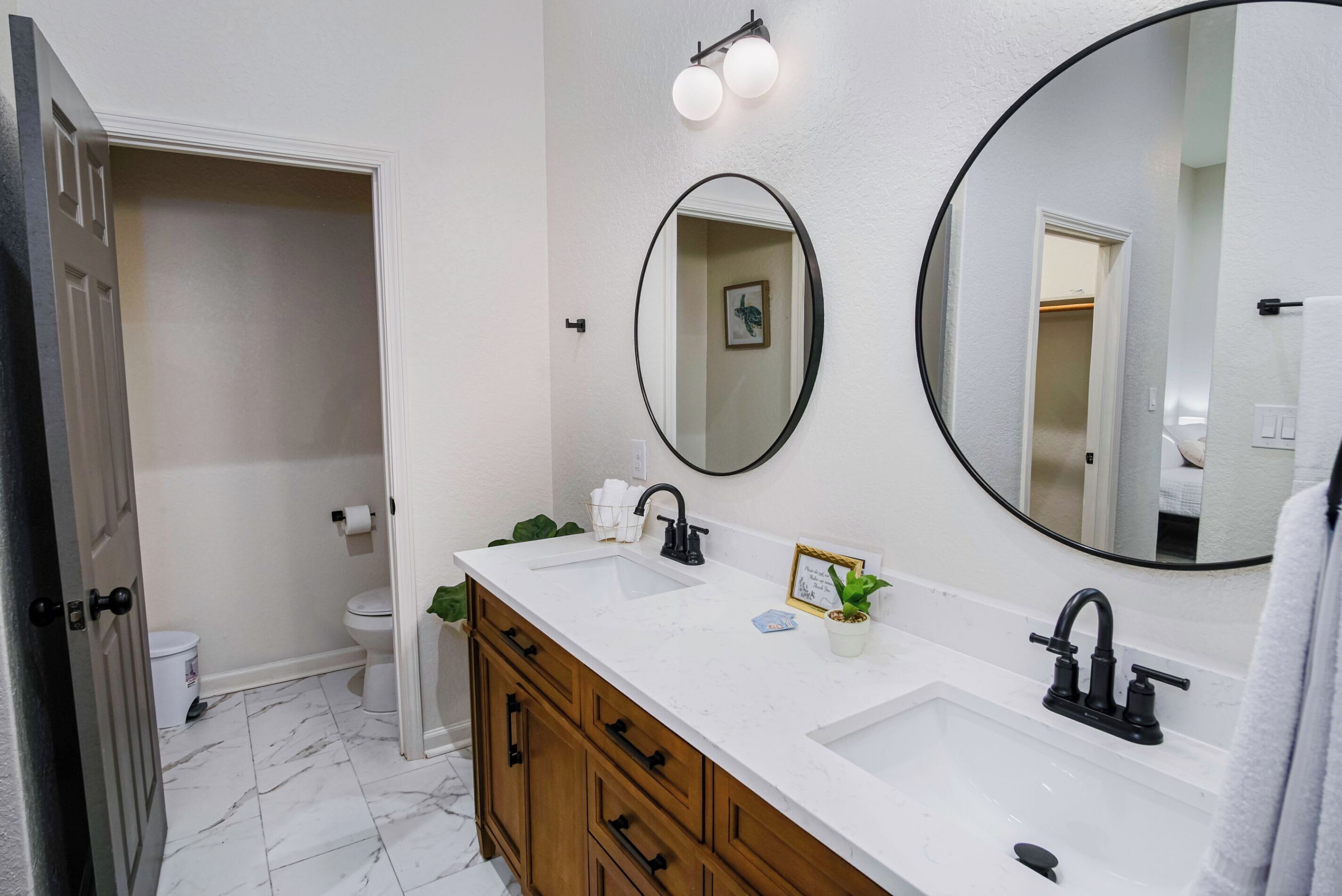 A bathroom with a white sink, two mirrors, a wooden vanity, and a toilet.