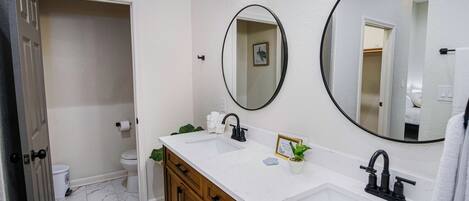 A bathroom with a white sink, two mirrors, a wooden vanity, and a toilet.
