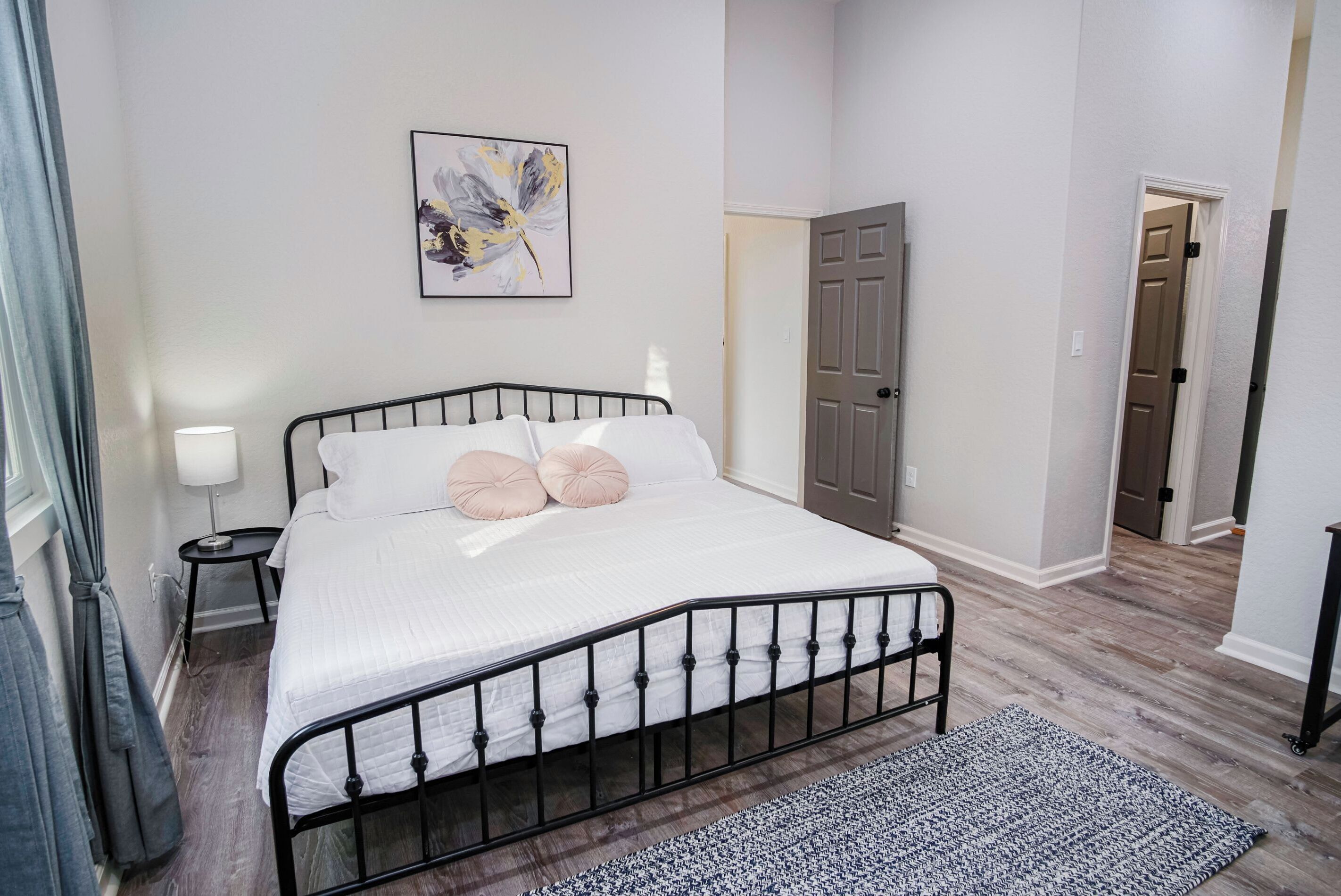 A bedroom with a bed, a nightstand, a lamp, a painting, and a door.