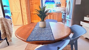 A modern kitchen with wooden cabinets, a stainless steel refrigerator, and a dining area with a round table and blue chairs. - Lakefront, Swim, Fish, Kayak, fire pit, star gazing, pet friendly. All on site! (New Market)