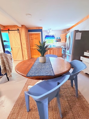 A modern kitchen with wooden cabinets, a stainless steel refrigerator, and a dining area with a round table and blue chairs.