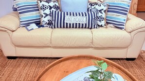 A beige sofa with striped and patterned cushions, a wooden coffee table with a plant and decorative plates, a chalkboard menu, and a wooden door with a barn-style design. - Lakefront, Swim, Fish, Kayak, fire pit, star gazing, pet friendly. All on site! (New Market)