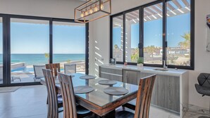 A modern dining area with a glass table, wooden chairs, and a view of the ocean. - Luxury Oceanfront Home with Pool & Hot Tub - located on Sandy Beach (Puerto Peñasco)