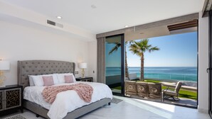 A bedroom with a large bed, a nightstand, a lamp, and a view of the ocean through a sliding door. - Luxury Oceanfront Home with Pool & Hot Tub - located on Sandy Beach (Puerto Peñasco)