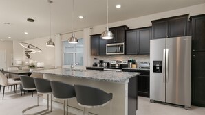 Una cocina moderna con armarios oscuros, electrodomésticos de acero inoxidable y una isla central con taburetes de bar.