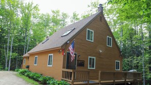 A wooden cabin with a porch, a flag, and a deck. - Freshly done, Quiet & very comfortable house in the heart of the White Mountains (Bartlett)