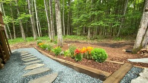 A garden pathway with stepping stones leading through a bed of gravel, surrounded by a wooden border and a variety of colorful flowers. - Freshly done, Quiet & very comfortable house in the heart of the White Mountains (Bartlett)