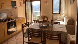 A cozy kitchen with wooden cabinets, a dining table set for four, and a view of mountains through the window. - 2 vacation apartments for up to 6 people, perfect for a vacation with family or friends (Idro)