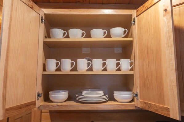 A wooden cabinet with multiple shelves containing white cups and bowls.