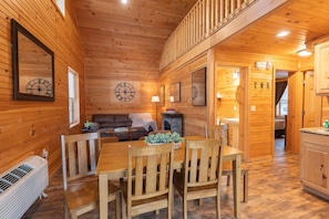 Interno di una baita in legno con tavolo da pranzo, sedie, divano e camino.