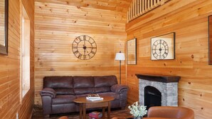 A cozy room with a wooden interior, featuring a leather sofa, a small table with a book, a lamp, and a fireplace.