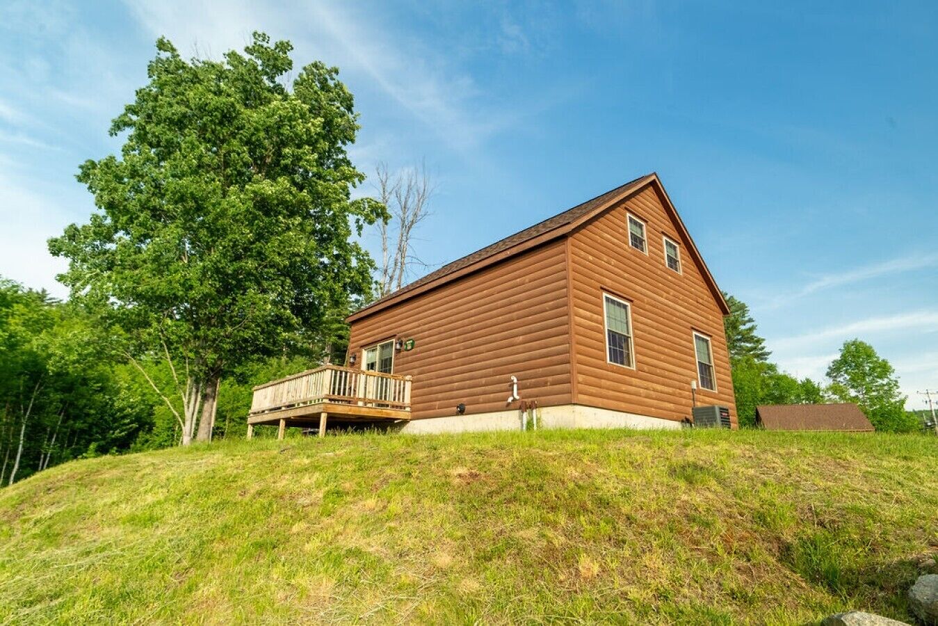 A wooden cabin with a deck, surrounded by trees and grassy terrain.