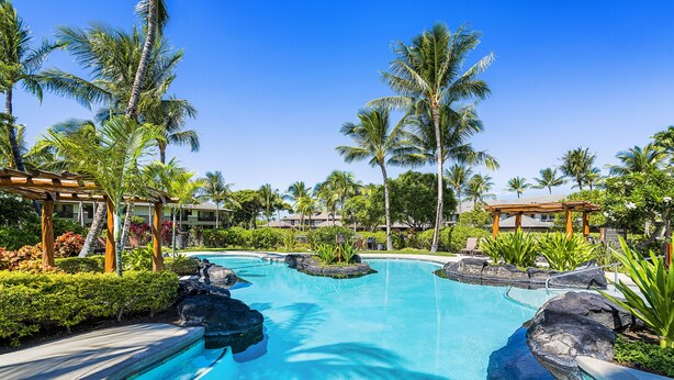 Ein Schwimmbecken mit Felsformationen, umgeben von Palmen und einer Holzpergola.