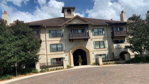 A large, multi-story building with a central entrance, balconies, and a paved driveway.