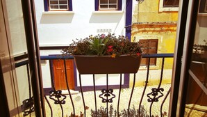 A balcony with potted plants and a view of a building with a white facade and blue diamond-shaped windows. - Aluguer apartamento Gaivota (Portimão)