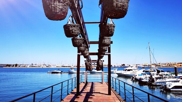 A wooden pier with a metal railing, leading to a marina with boats docked. - Aluguer apartamento Gaivota (Portimão)