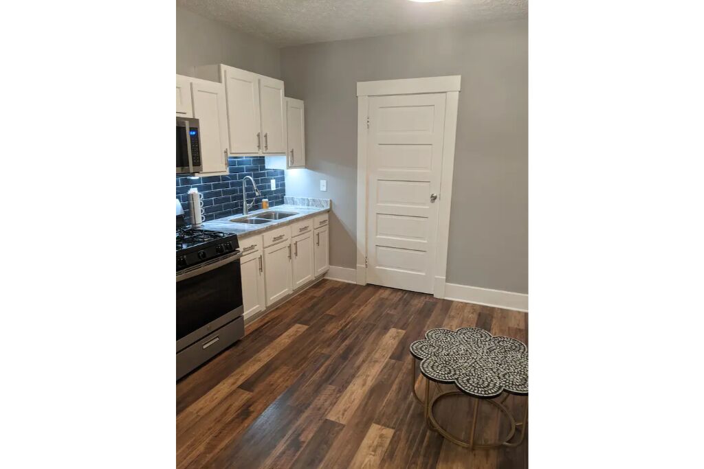 A kitchen with white cabinets, a stainless steel stove, and a blue tiled backsplash.