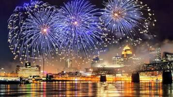 A city skyline with fireworks over a body of water, reflecting city lights.