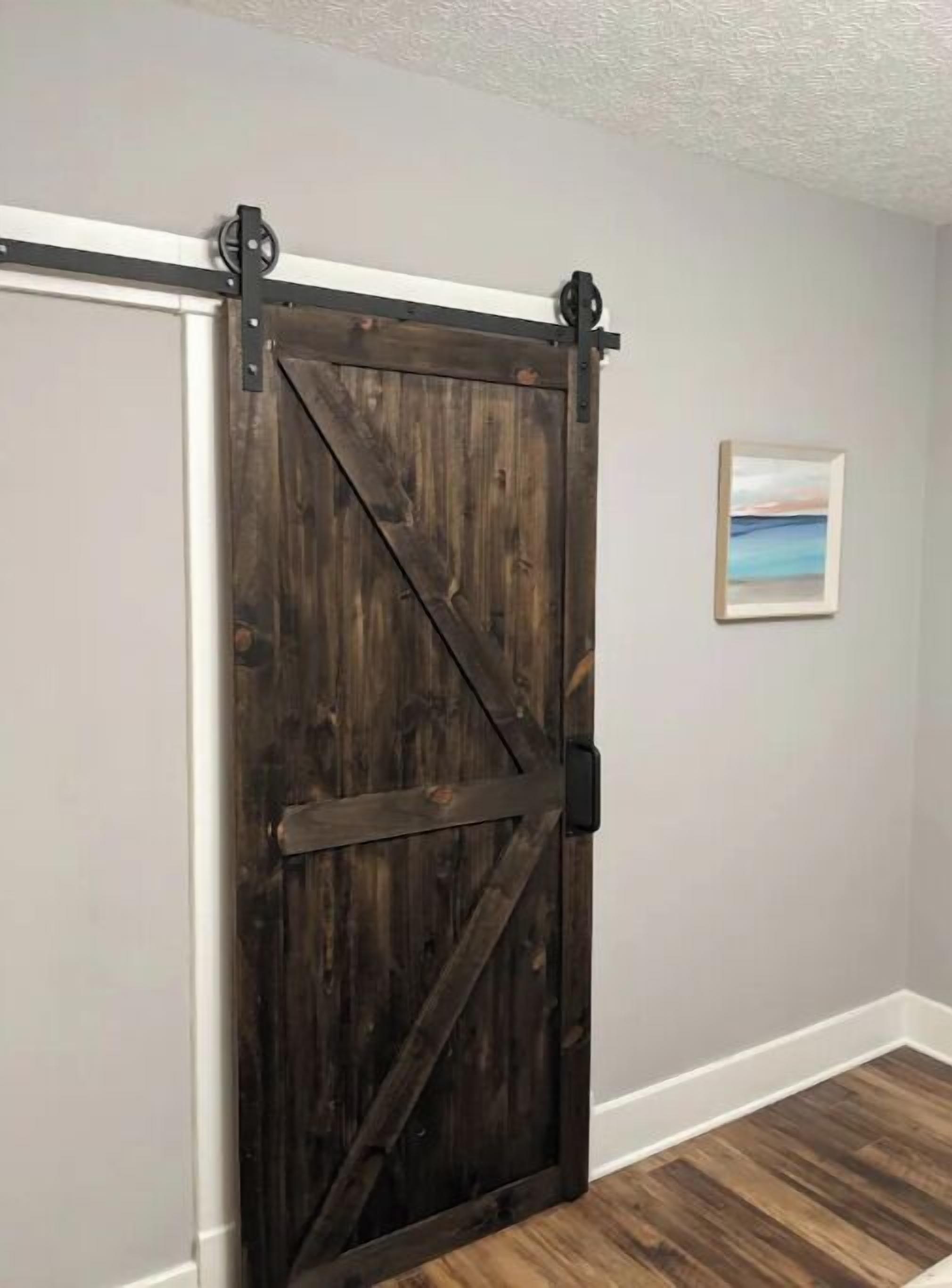 A dark wooden barn-style sliding door with metal hardware, white trim, and a framed picture on the wall.
