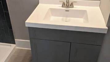Un bany amb un lavabo blanc, mobles fosc grisos i una banyera.